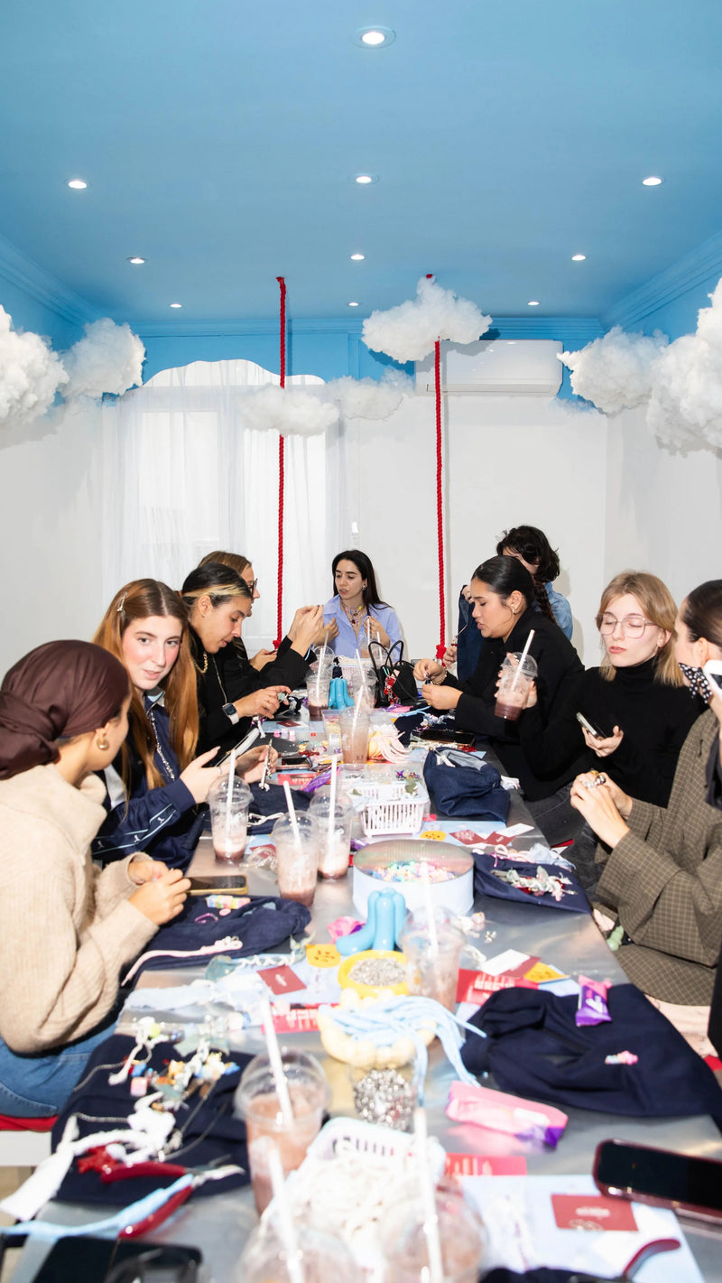 A group of friends making jewelry together at the long table in the Cloud Room at Cherry PaoPao in Brussels, with clouds hanging from the blue ceiling